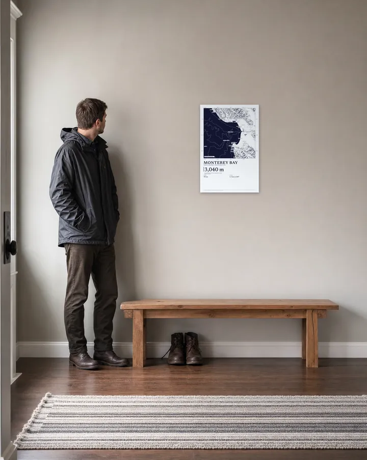 Generated scene: an entrance hall, above a low bench. On the wall, our real Linocut drawing of Monterey Bay at 16 × 24 in, set at true scale beside a man 5 ft 10 in tall.