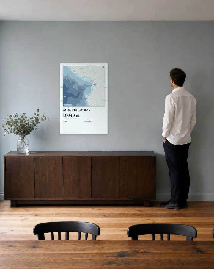 Generated scene: a dining room, above a sideboard. On the wall, our real Bathymetric drawing of Monterey Bay at 24 × 36 in, set at true scale beside a man 5 ft 11 in tall.