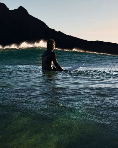 Generated scene: a surfer sitting on a board at first light, the water darkening where the bottom drops away.